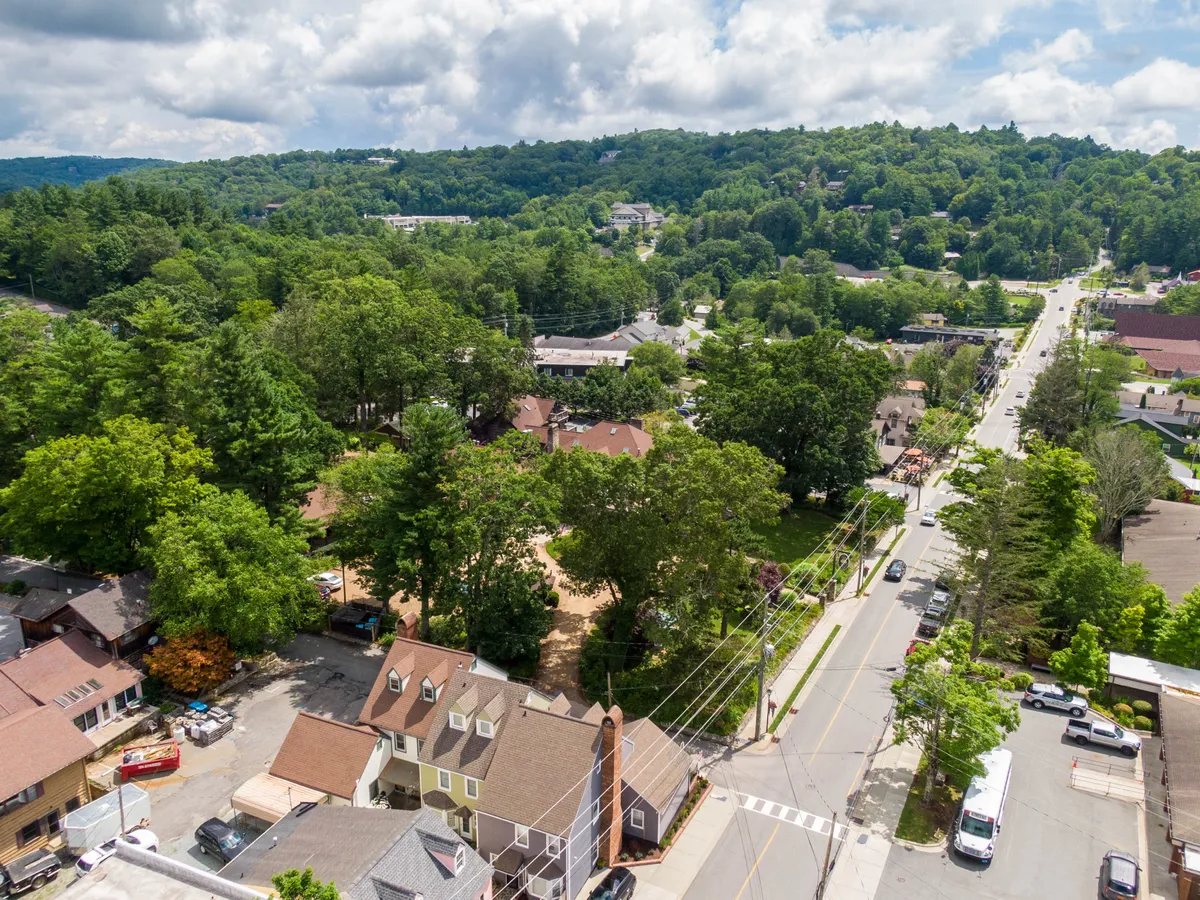 A scenic neighborhood view of lush greenery, residential homes, and a winding road, capturing the charm and vibrancy of the Blowing Rock community. The perspective highlights the walkable, picturesque environment just outside the inn.