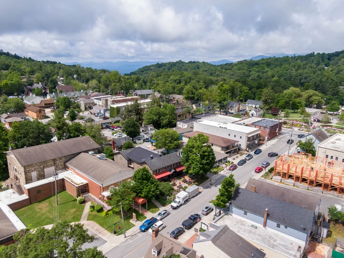 A sweeping view of Blowing Rock’s charming town square, framed by tree-lined streets and backed by rolling mountains. Various buildings—including shops and restaurants—line the streets, bustling with activity. The lively vibe of the town center is evident, inviting visitors to explore and enjoy the local scene.