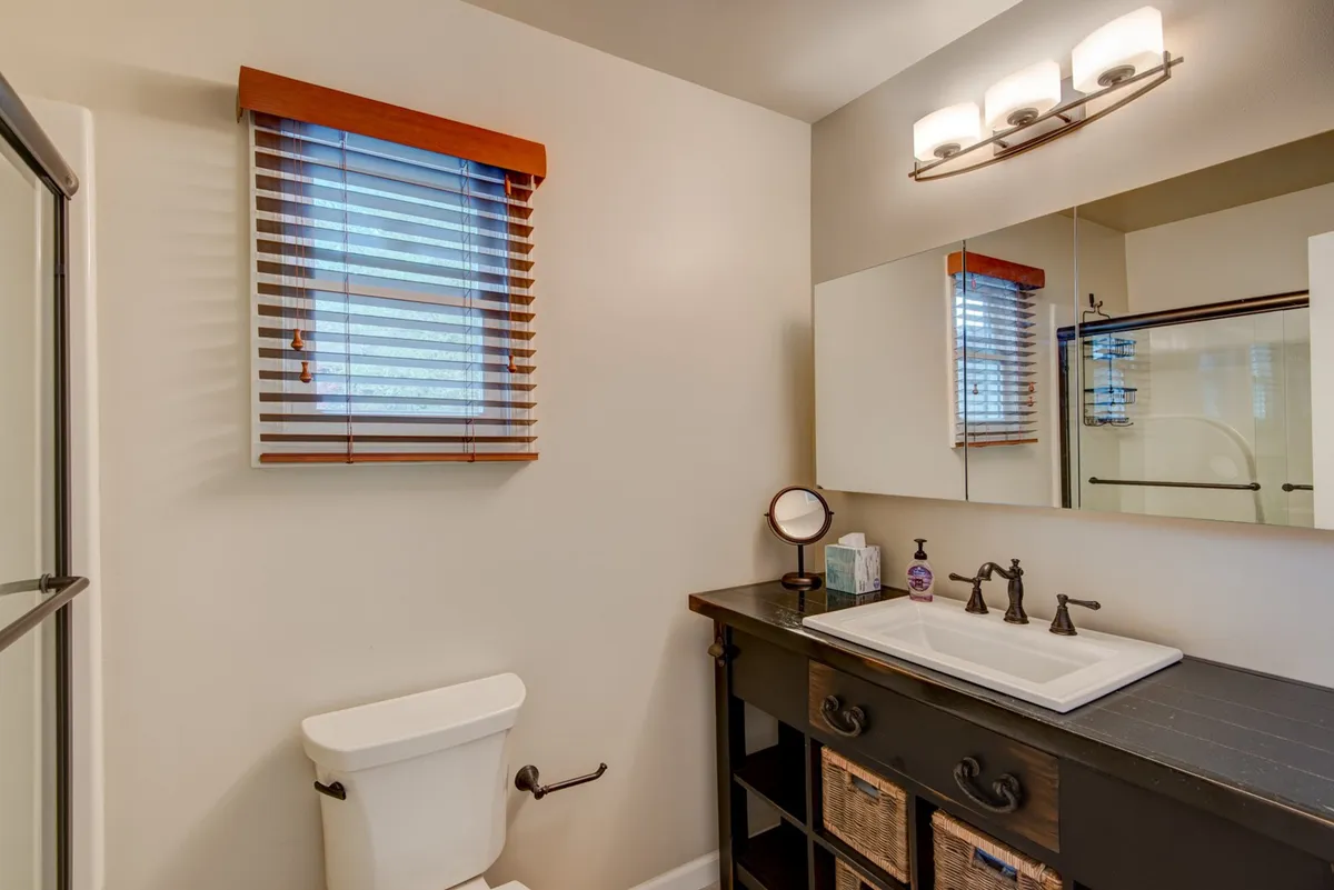 A light-filled half bath with a modern sink, large mirror, and a window with blinds. The clean, refreshing design makes it a practical and pleasant space for guests to freshen up.